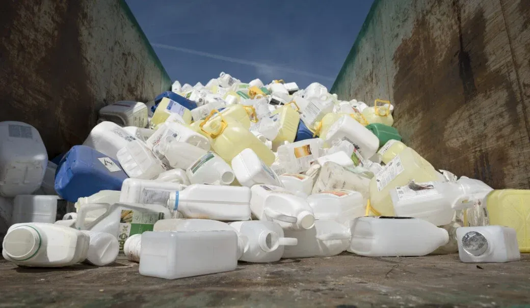Ein Haufen Plastikkannen, Flaschen und Behälter sind in einen Recyclingbehälter gekippt. Einige sind leer, andere haben Etiketten.
