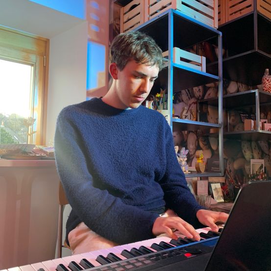 Ein Mann in einem blauen Pullover spielt Klavier in einem Raum.