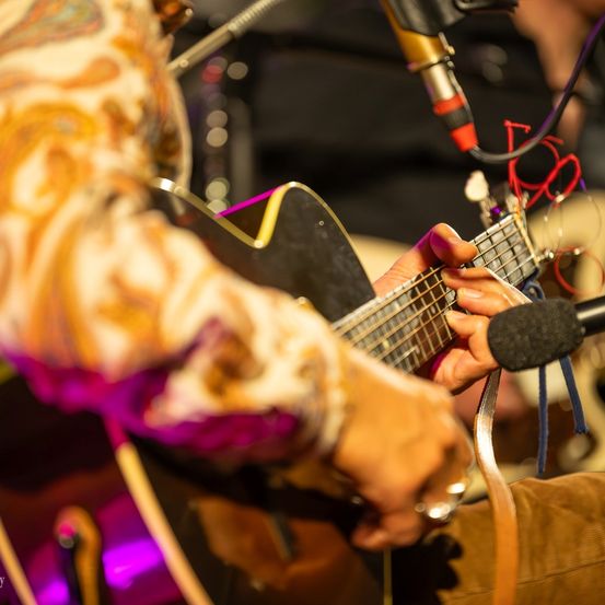 Ein Musiker spielt eine Gitarre unter einem lila Licht mit einem Mikrofon davor.