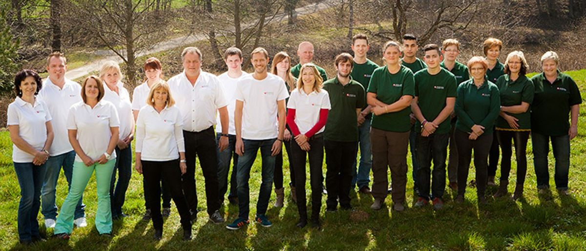 Eine Gruppe von Menschen in grünen und weißen Hemden steht auf einer Wiese mit Bäumen im Hintergrund.