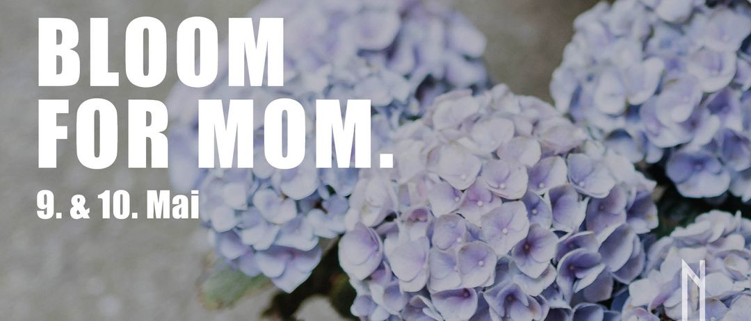 Ein Strauß lilafarbener Blumen mit dem Wort 'Mom' darauf geschrieben. Die Blumen sind verschwommen, einige sind in voller Blüte und andere nicht. Die Blätter sind grün.