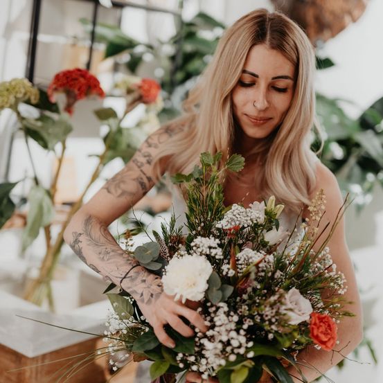 Eine Frau mit Tätowierungen auf den Armen hält einen Blumenstrauß, möglicherweise für eine Hochzeit.