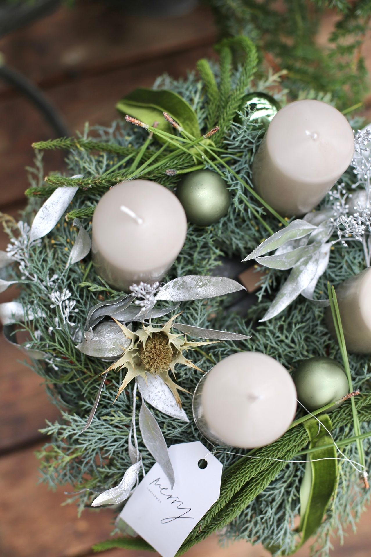 Ein Kranz mit fünf Kerzen, grünen Blättern und silbernen und grünen Ornamenten. Die Kerzen sind weiß und der Kranz hat einen natürlichen Look.