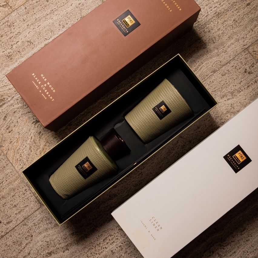 Eine braune Schachtel mit 'Exclusive' und 'Eiche-Holz Schwarze Johannisbeere' darauf geschrieben. Eine kleinere Schachtel enthält zwei Kerzen in Schwarz und Grün. Eine weiße Schachtel mit 'Saubere Wäsche' darauf geschrieben.