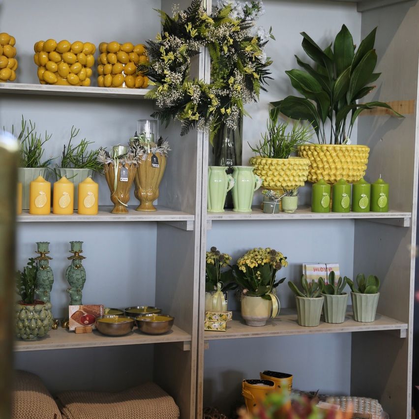 A display of decorative items in a store, featuring yellow and green vases, potted plants, and lemon-shaped candles on shelves.