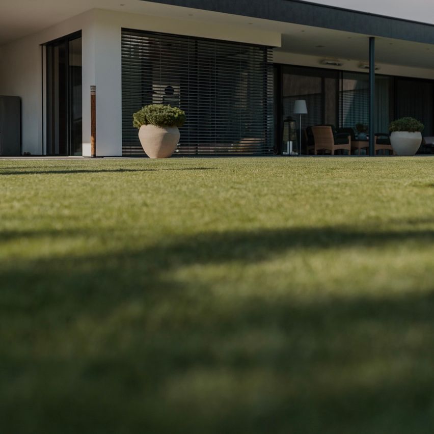 A modern house with large windows, potted plants outside, and a green lawn in the foreground.