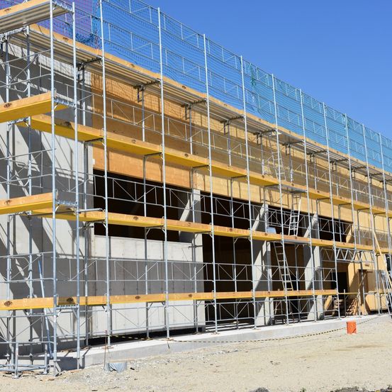Ein laufendes Baustelle mit Metallgerüsten und gelben Tafeln an einem sonnigen Tag.