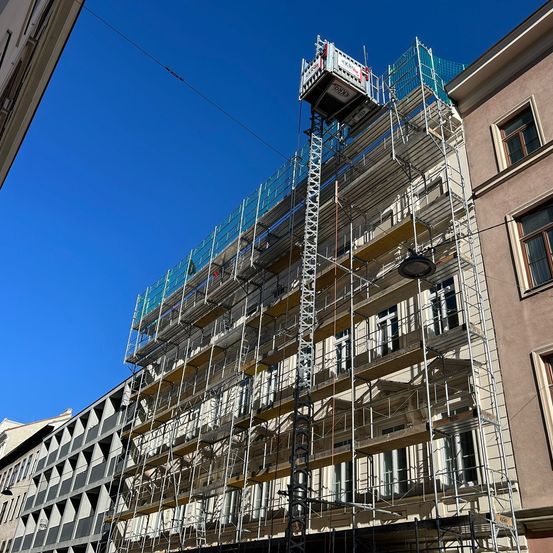Ein hohes Gebäude mit einer Gerüstkonstruktion in der Stadt. Das Gerüst hat eine Metallleiter und eine Metallplattform mit einem roten Kasten oben.