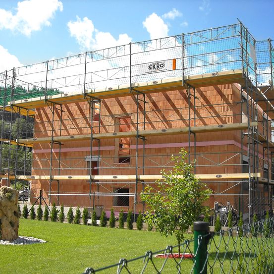 Eine Baustelle mit einem Gebäude im Bau. Das Gebäude hat Ziegelwände und ist von Metallgerüsten umgeben.