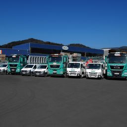 Eine Reihe grüner und weißer Fahrzeuge, die vor einem blauen Gebäude mit der Aufschrift 'EKRO' geparkt sind.