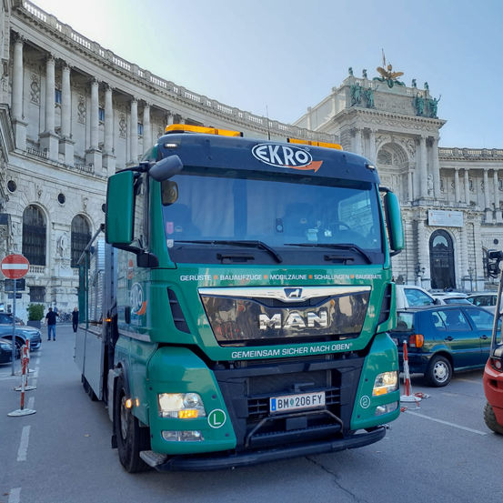 Ein grüner LKW mit dem Logo und dem Wort 'Ekro' auf der Vorderseite ist vor einem großen Gebäude mit vielen Säulen geparkt.