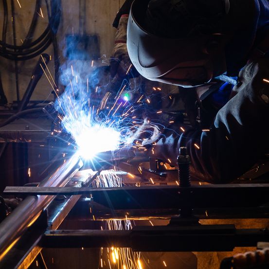 Ein Schweißer mit Schweißerhelm schweißt einen Metallrohr in einer Werkstatt.