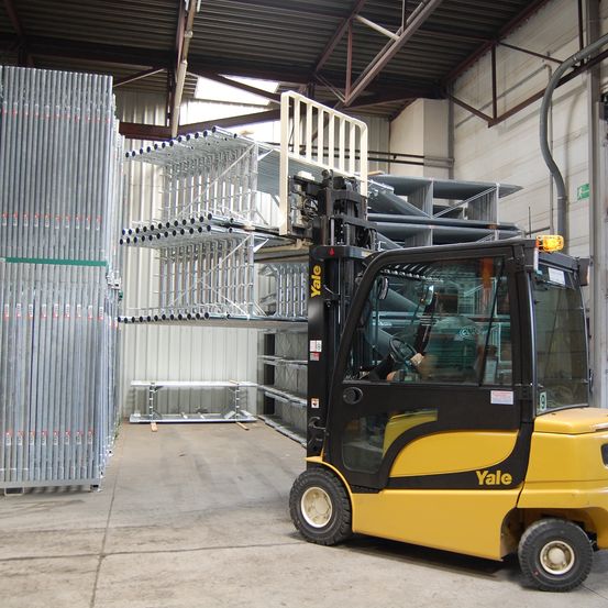 Gelber Gabelstapler mit dem Yale-Logo fährt in ein Lager mit einer Palettenregale im Hintergrund.