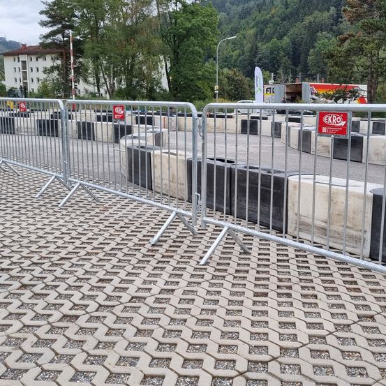Eine Metallbarriere steht auf einem Betonboden mit sechseckigem Muster. Es gibt Barrieren am Straßenrand.