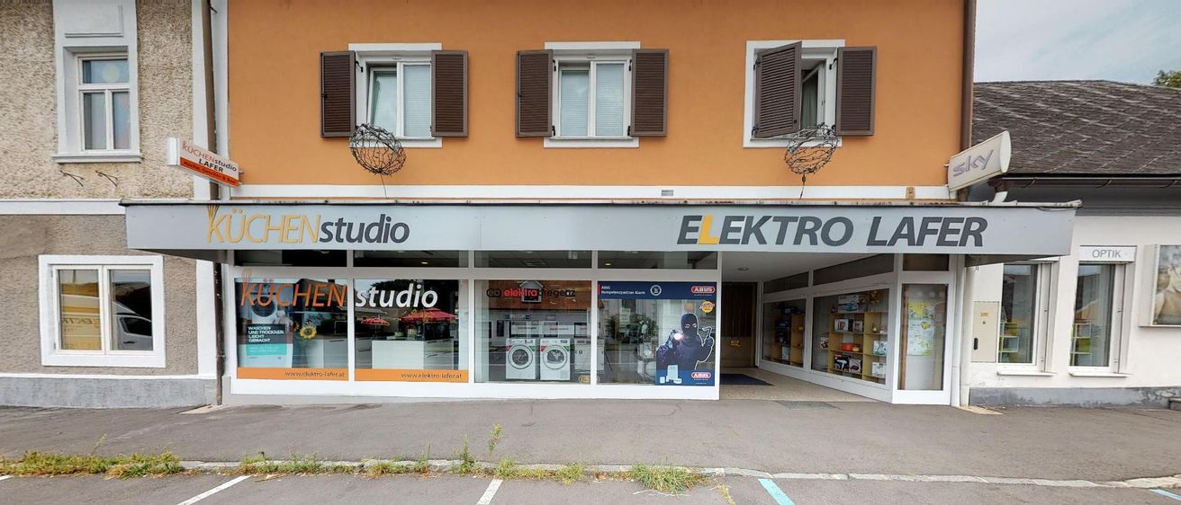 Die Fassade eines Elektrogeräte-Geschäfts mit dem Namen Elektro Läferat. Es zeigt ein Glasfenster mit Waschmaschinen und einem Poster eines Mannes.