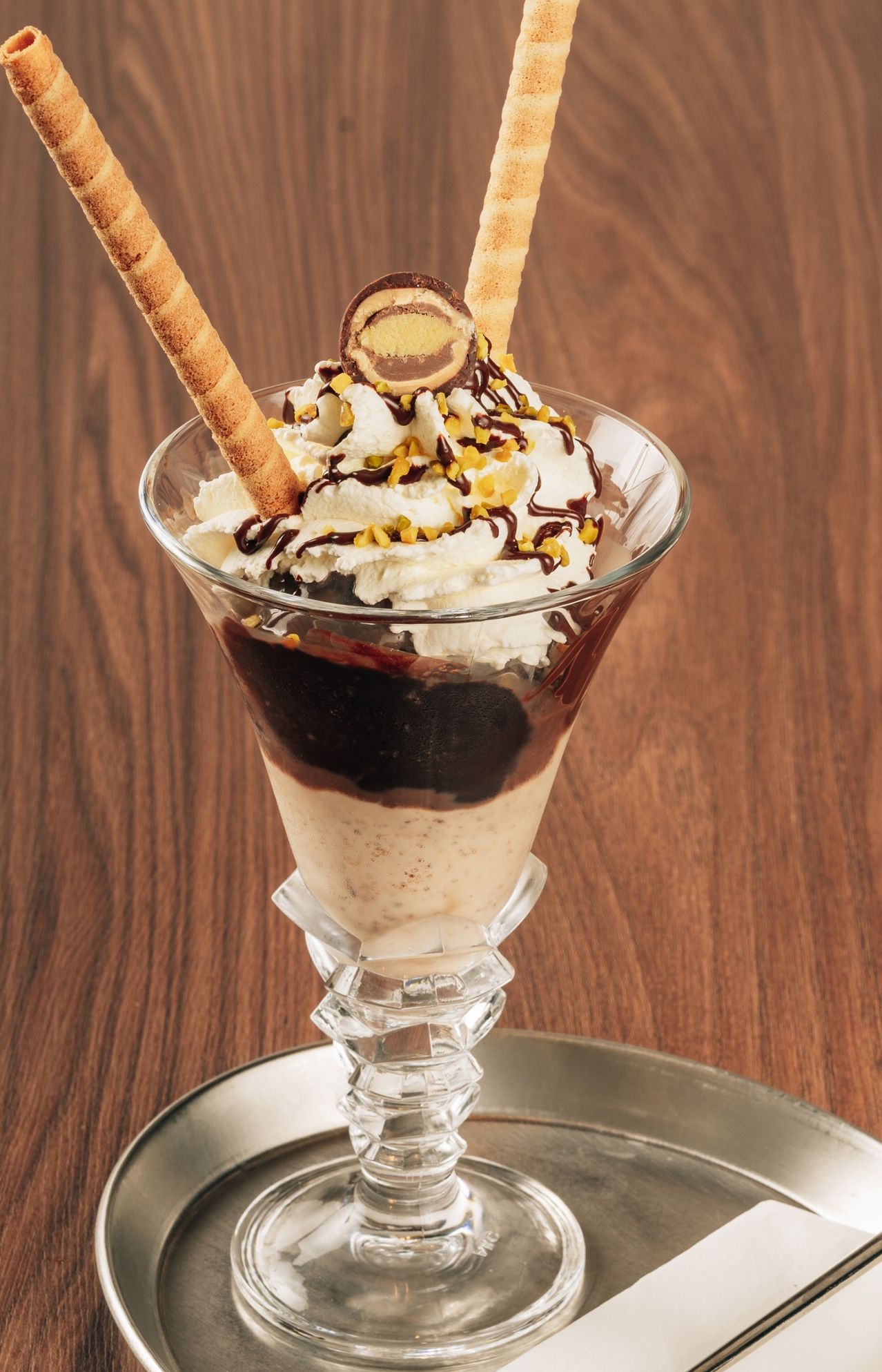 Ein Glas Eisbecher mit Schokoladeneis, Schlagsahne, Schokoladensauce und einem Kekswirbel obenauf.
