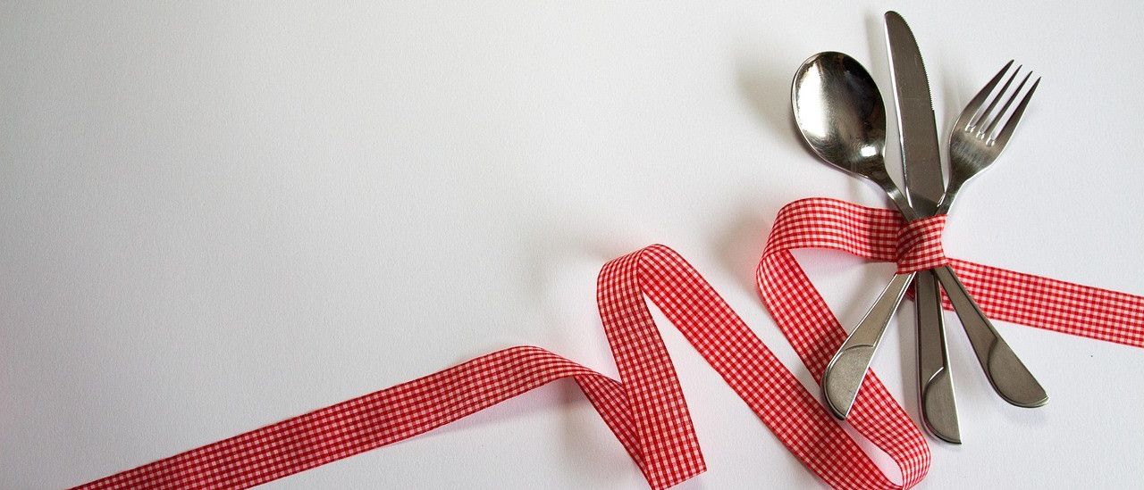 Ein rotes Band verbindet ein Messer, einen Löffel und eine Gabel auf weißem Hintergrund. Das Band und das Besteck sind reflektierend und verleihen einen dekorativen Touch.