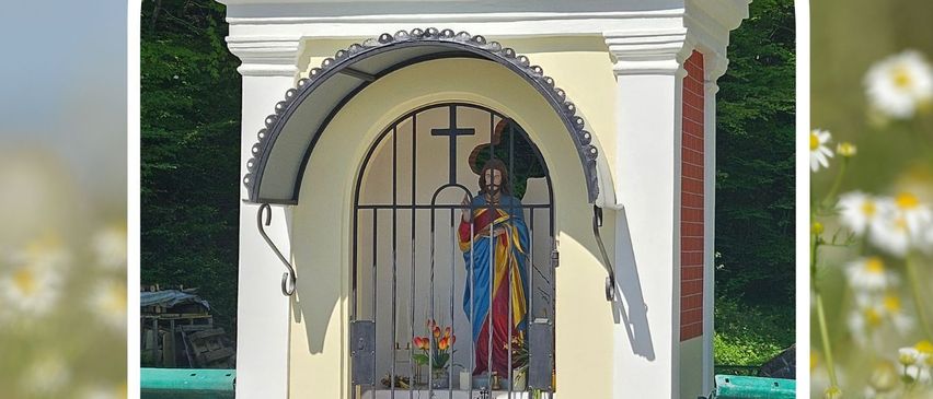 Eine kleine Kapelle mit einer Statue im Inneren, umgeben von Blumen und Grün. Die Kapelle hat ein Kreuz und das Jahr 1854. Sie ist renoviert und für den Gottesdienst geöffnet.