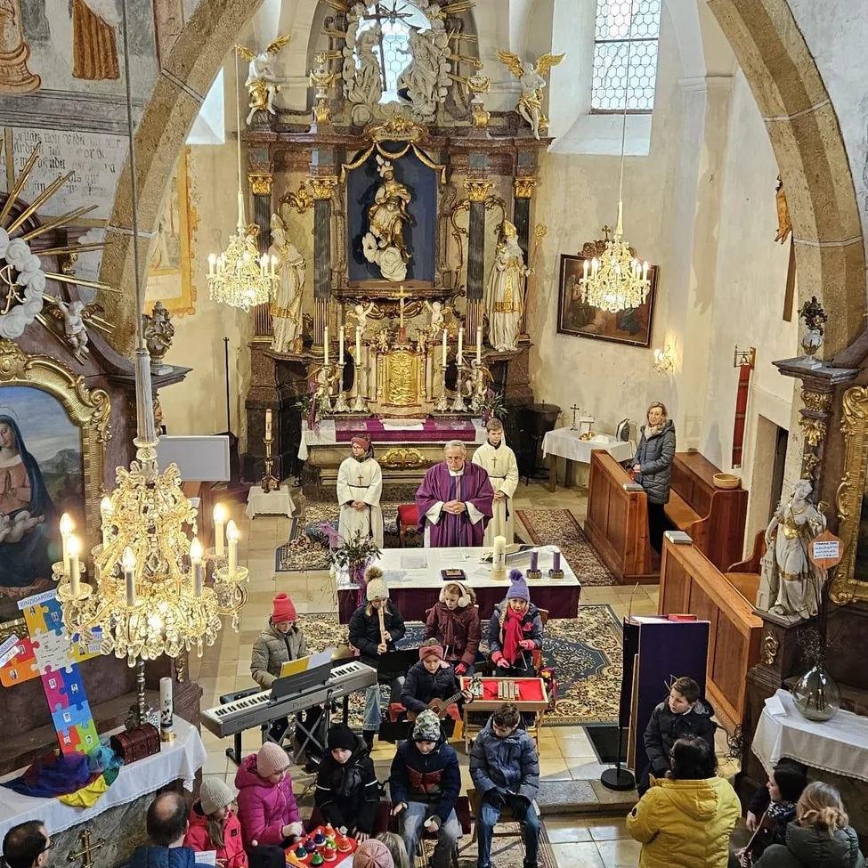 Eine religiöse Zeremonie in einer Kirche mit einem Priester in Purpur, der anführt, einem Chor und einer Gemeinde, die auf dem Boden sitzen. Altar, Kerzen und Statuen sind vorhanden.