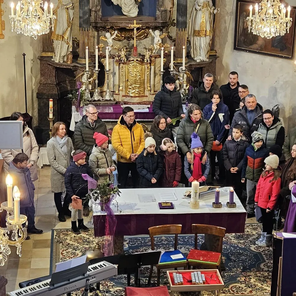Eine Gruppe von Erwachsenen und Kindern steht um einen Altar in einer Kirche, Kerzen und religiöse Gegenstände sind vorhanden.