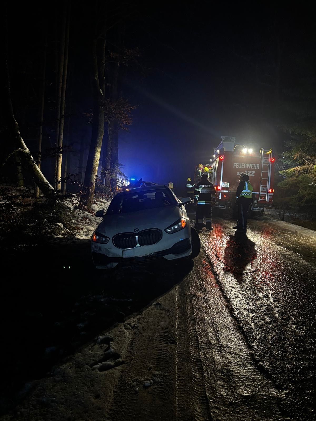 Bei Nacht ist ein BMW-Auto auf einer Straße verunglückt. Rettungsdienste kümmern sich um den Vorfall, mit einem Feuerwehrwagen und Polizeiauto in der Nähe.