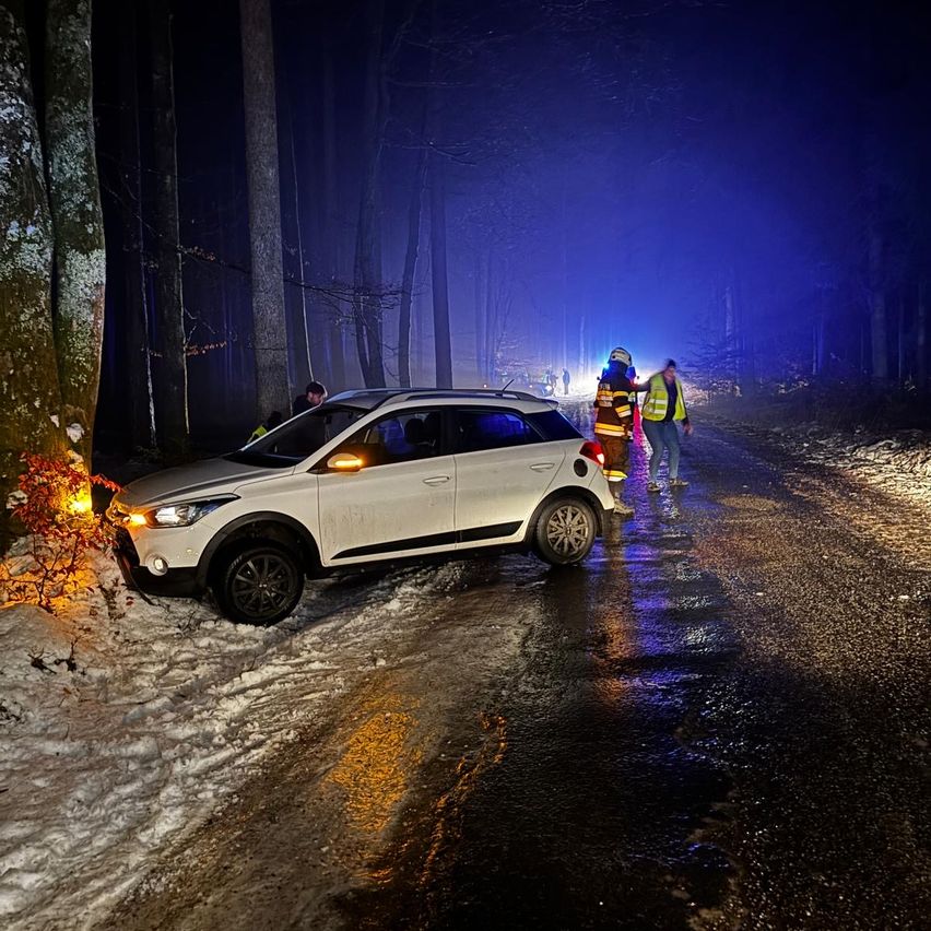 Ein weißer SUV ist auf einer verschneiten Straße bei Nacht geparkt, von einem Baum getroffen. Rettungskräfte sind vor Ort.