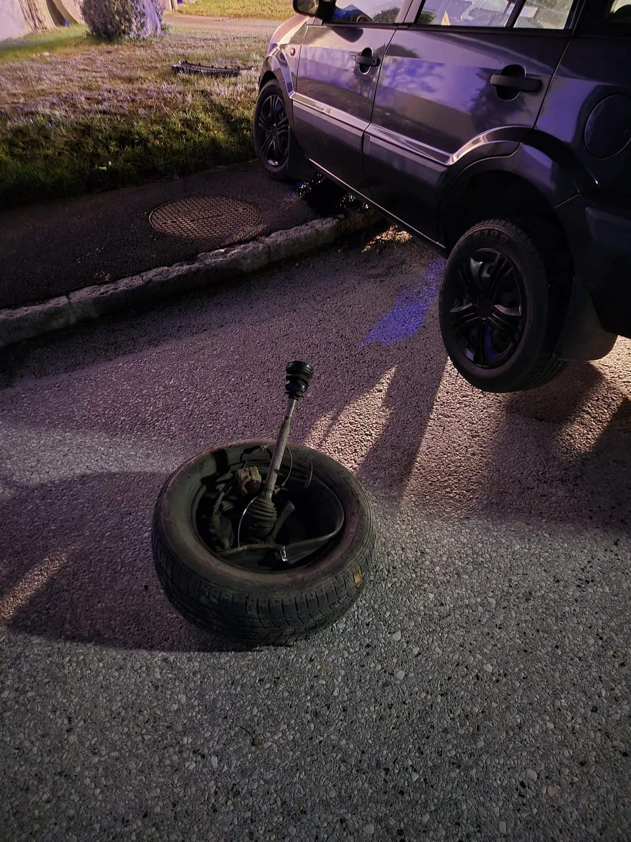 Ein Auto mit einem platten Reifen am Straßenrand bei Nacht, mit abgekoppeltem Rad.