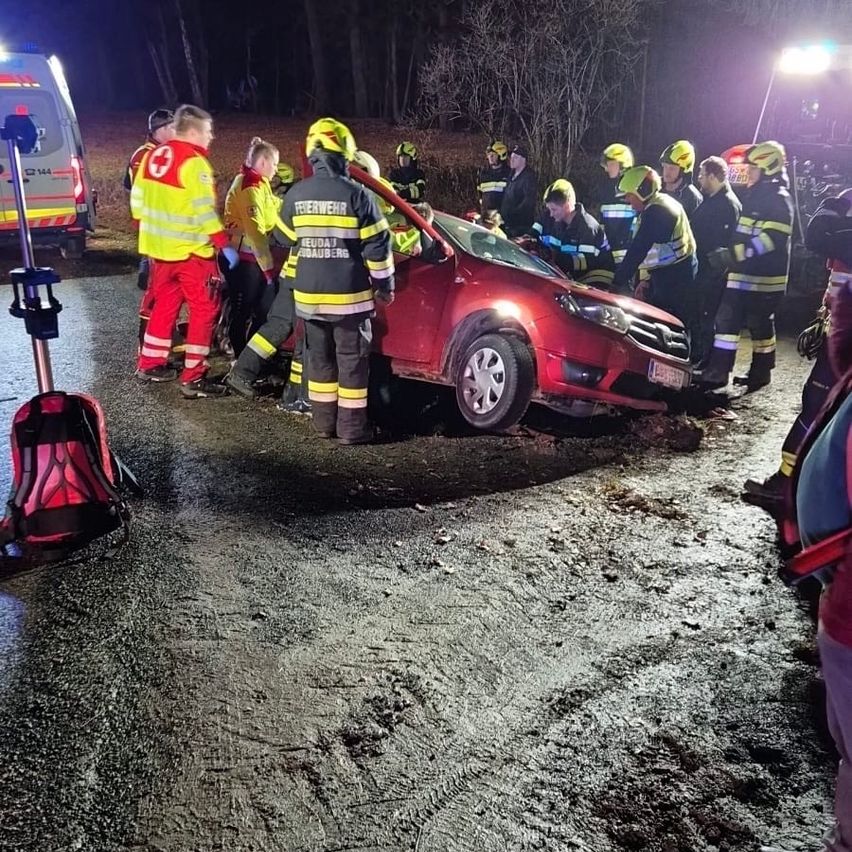 Emergency responders in yellow and red uniforms assist a red car crash victim at night. Vehicles and trees surround the scene.