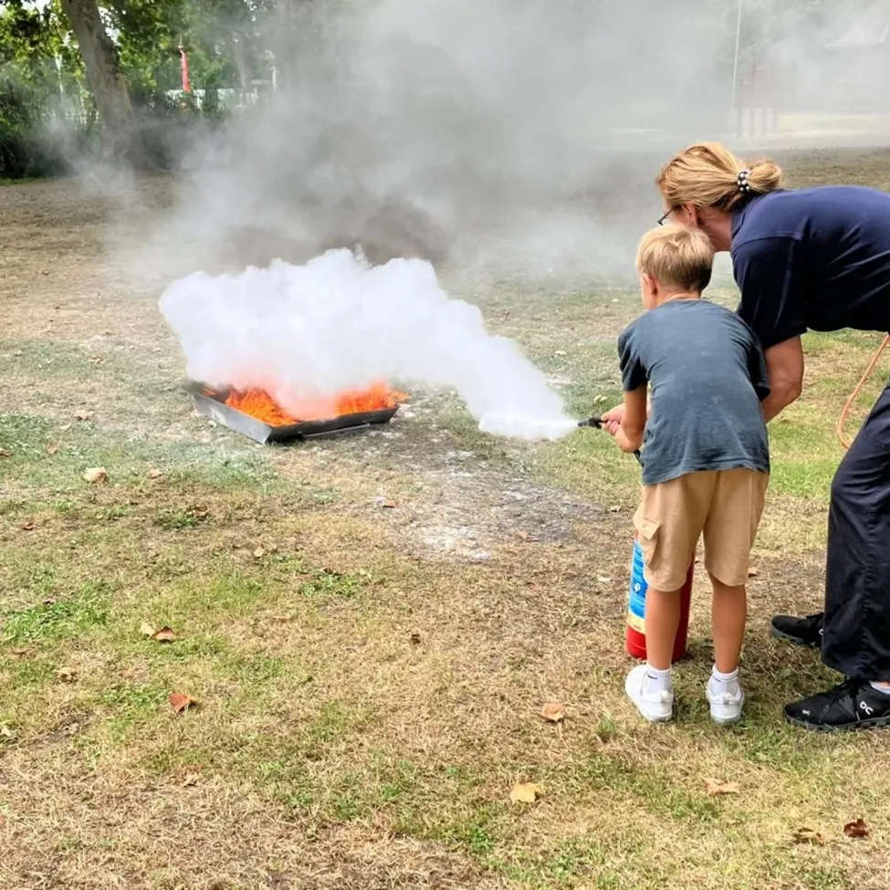 Eine Frau und ein Junge verwenden einen Feuerlöscher, um ein kleines Feuer auf einem Metalltablett in einem Park zu löschen.