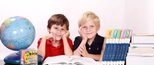 Zwei Jungen sitzen an einem Schreibtisch mit einem offenen Buch, Malstiften und einem Globus. Einer trägt ein rotes Shirt, der andere ein schwarzes. Dahinter sind mehrere Childcraft-Bücher ordentlich aufgereiht.