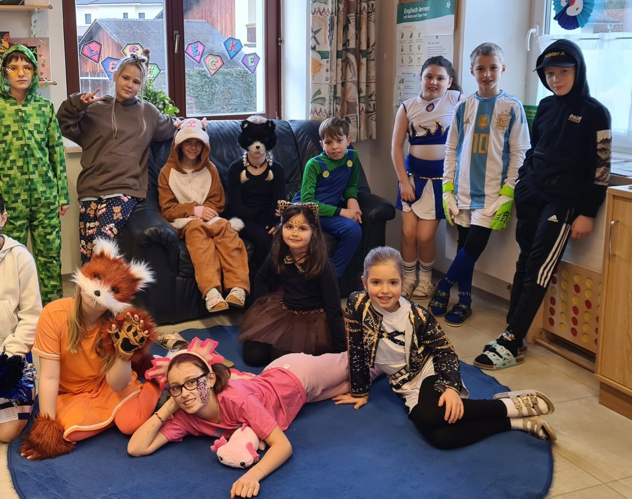 Gruppe von Kindern in verschiedenen Kostümen posiert drinnen. Einige sitzen auf einer Couch, andere auf einem blauen Teppich. Ein Kind trägt ein Fuchskostüm und ein anderes ein Fußballtrikot.