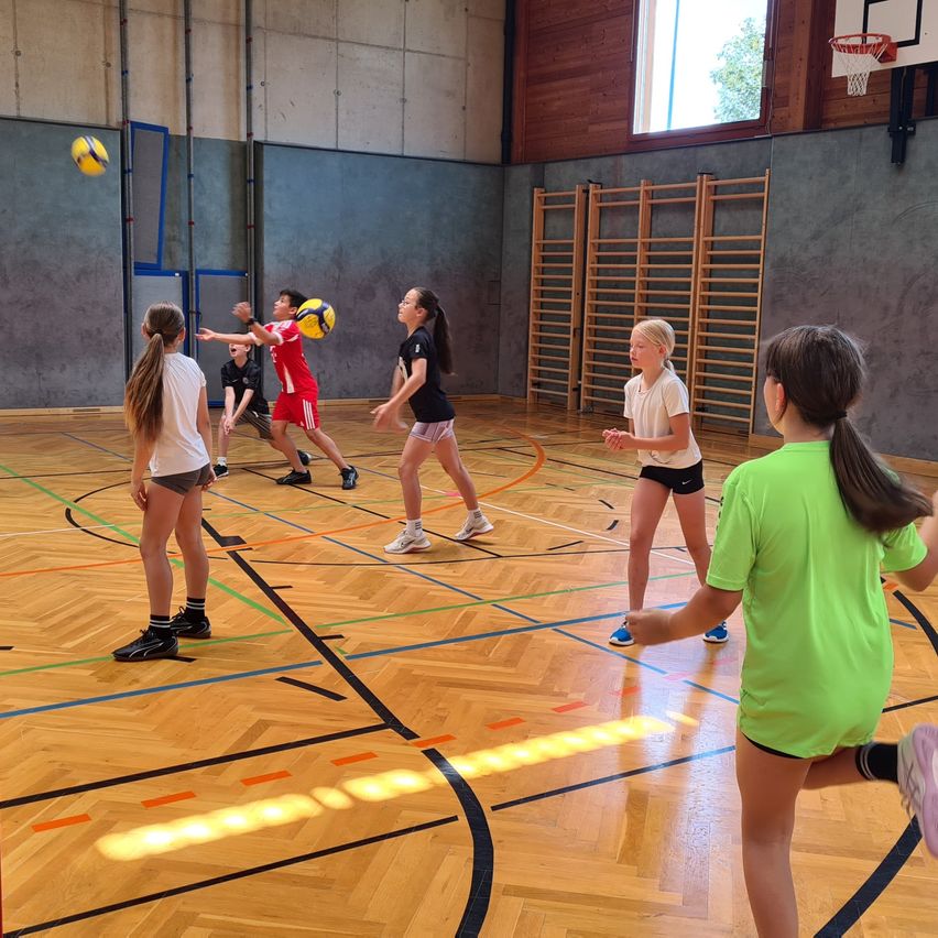 Eine Gruppe von Mädchen spielt Volleyball in einer Turnhalle. Ein Mädchen in Grün ist dabei, den Ball zu schlagen.