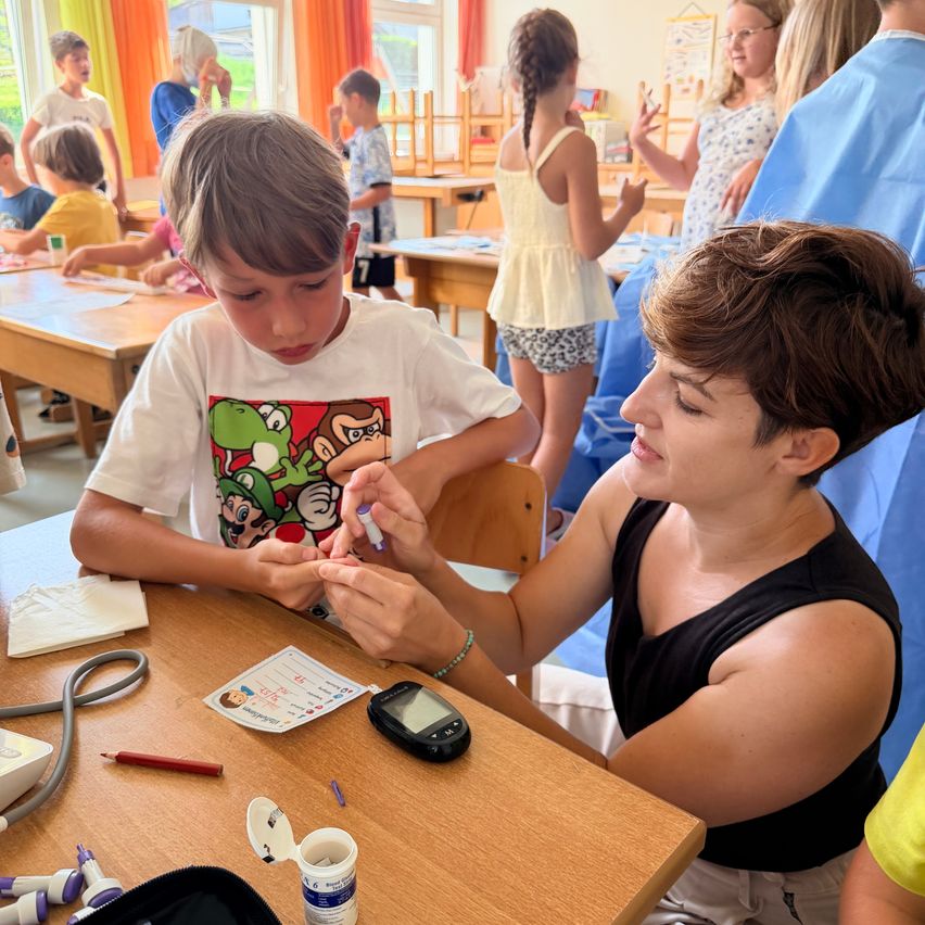 A woman is checking a young boy's blood sugar level with a glucometer in a classroom setting.