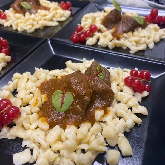 Ein Nahaufnahme eines Tellers mit Nudeln, roten Beeren und einem Fleischgericht. Die Nudeln sind mit einer braunen Sauce überzogen, und es gibt rote Beeren an der Seite.