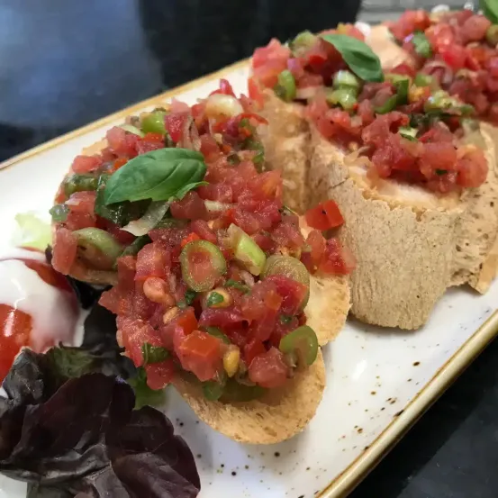 Ein Teller mit Bruschetta, belegt mit gewürfelten Tomaten, Frühlingszwiebeln und Basilikumblättern.