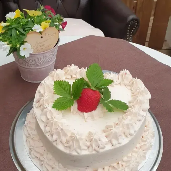 Ein weißer Kuchen mit Schlagsahne und einer Erdbeere darauf, neben einem Blumentopf auf einem Tisch.