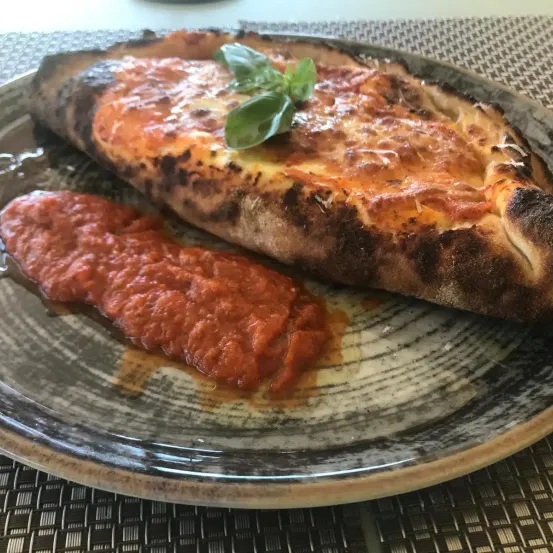 Eine Pizza mit geschmolzenem Käse und Basilikumblättern auf einem Teller mit einer Beilage von roter Sauce.