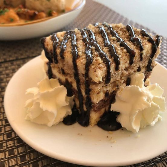 Ein Stück Kuchen mit Schokoladenglasur und Schlagsahne auf einem weißen Teller.