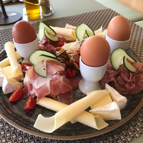 Ein Teller mit verschiedenen Frühstücksartikeln, darunter Eier, Käse, Gurken und Fleisch.