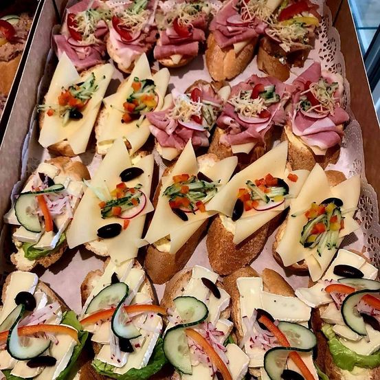 Eine Schachtel mit verschiedenen Sandwiches mit unterschiedlichen Belägen wie Käse, Gemüse und Fleisch auf einem weißen Tuch.