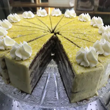 Ein geschnittener gelber Kuchen mit weißer Schlagsahne obenauf, auf einem Glaskuchenständer.