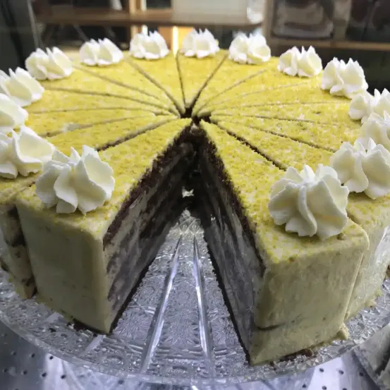 Ein geschnittener gelber Kuchen mit weißer Schlagsahne obenauf, auf einem Glaskuchenständer.