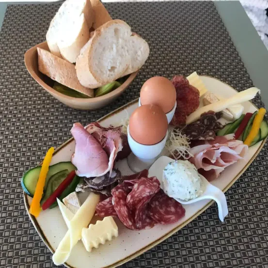 Ein Frühstücksplatten mit Eiern, Schinken, Käse, Brot und Gemüse auf einem Tisch.