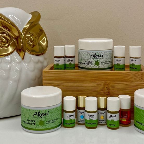 Eine Sammlung von Hautpflegeprodukten von Akari, einschließlich verschiedener Cremes, Seren und einer golden akzentuierten Eulenfigur.