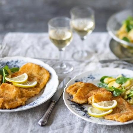 Zwei Teller mit frittierten Speisen mit Zitronenscheiben und Weingläsern auf einem Tisch. Ein Teller hat ein Messer daneben.