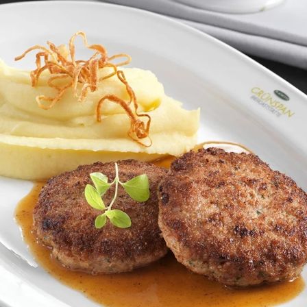 Zwei Fleischpatties mit grüner Garnierung auf einem Teller, begleitet von Kartoffelpüree und brauner Sauce.