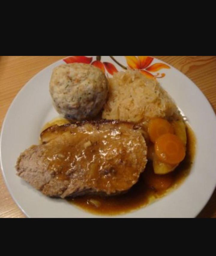 Ein Teller mit traditionellem deutschem Essen mit einer Fleischkugel, Sauerkraut und Fleisch, bedeckt mit Soße, auf einer Holzoberfläche.