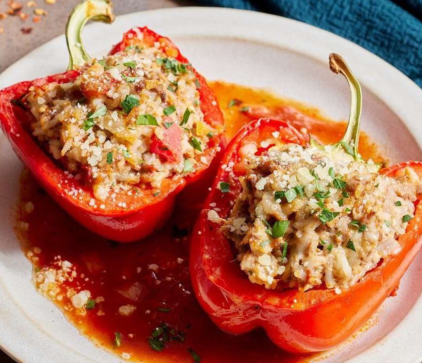 Two red bell peppers stuffed with a mixture of cheese, herbs, and possibly meat, on a plate with red sauce.