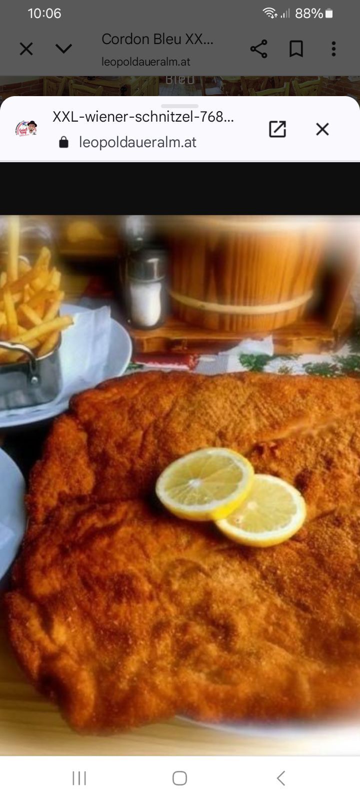 Ein goldenes gebratenes Fischfilet mit zwei Zitronenscheiben auf einem Teller, begleitet von einer Schale Pommes Frites und einem hölzernen Fass im Hintergrund.