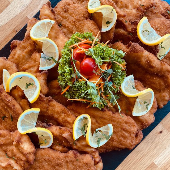 Eine Platte mit knusprigen gebratenen Schnitzeln, einer Salatmischung aus Grünzeug und Karotten, verziert mit Zitronenscheiben, auf einer blauen Oberfläche.